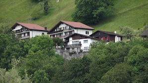 A cluster of chalet-style buildings with red roofs, surrounded by dense greenery and hills.