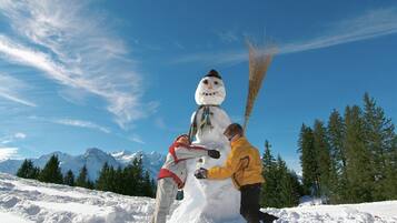 Un bonhomme de neige tenant un balai, et une personne vêtue d’une veste jaune, debout à côté de lui.