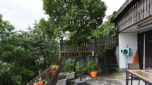 A patio with a wooden fence, potted plants, a garden hose, and a bench.