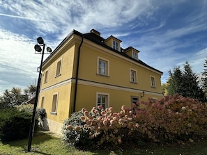 A two-story yellow building with a symmetrical facade, multiple windows, and a visible chimney.