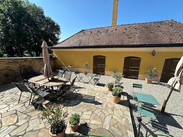 A courtyard with outdoor seating, potted plants, and a yellow building with wooden doors.
