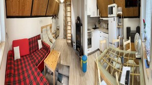 A compact living space with a sofa, a small table, a kitchen area with a microwave and a TV, and a glass dining table.