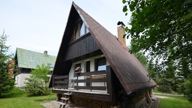A traditional chalet with a steep roof, stone foundation, and a wooden deck.