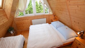 A cozy wooden cabin bedroom with a large bed, a bedside table, and a window with curtains.