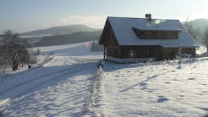 Een houten hut met een schuin dak, omgeven door een met sneeuw bedekte grond en een heldere lucht.