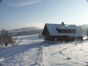 A wooden cabin with a sloped roof, surrounded by snow-covered ground and a clear sky.