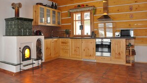 Een houten blokhut interieur met een open haard, houten keukenkastjes, een magnetron en een betegelde vloer.