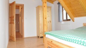 Een kamer met een houten plafond, een bed met een geruit beddegoed, een kledingkast en een raam met gordijn.
