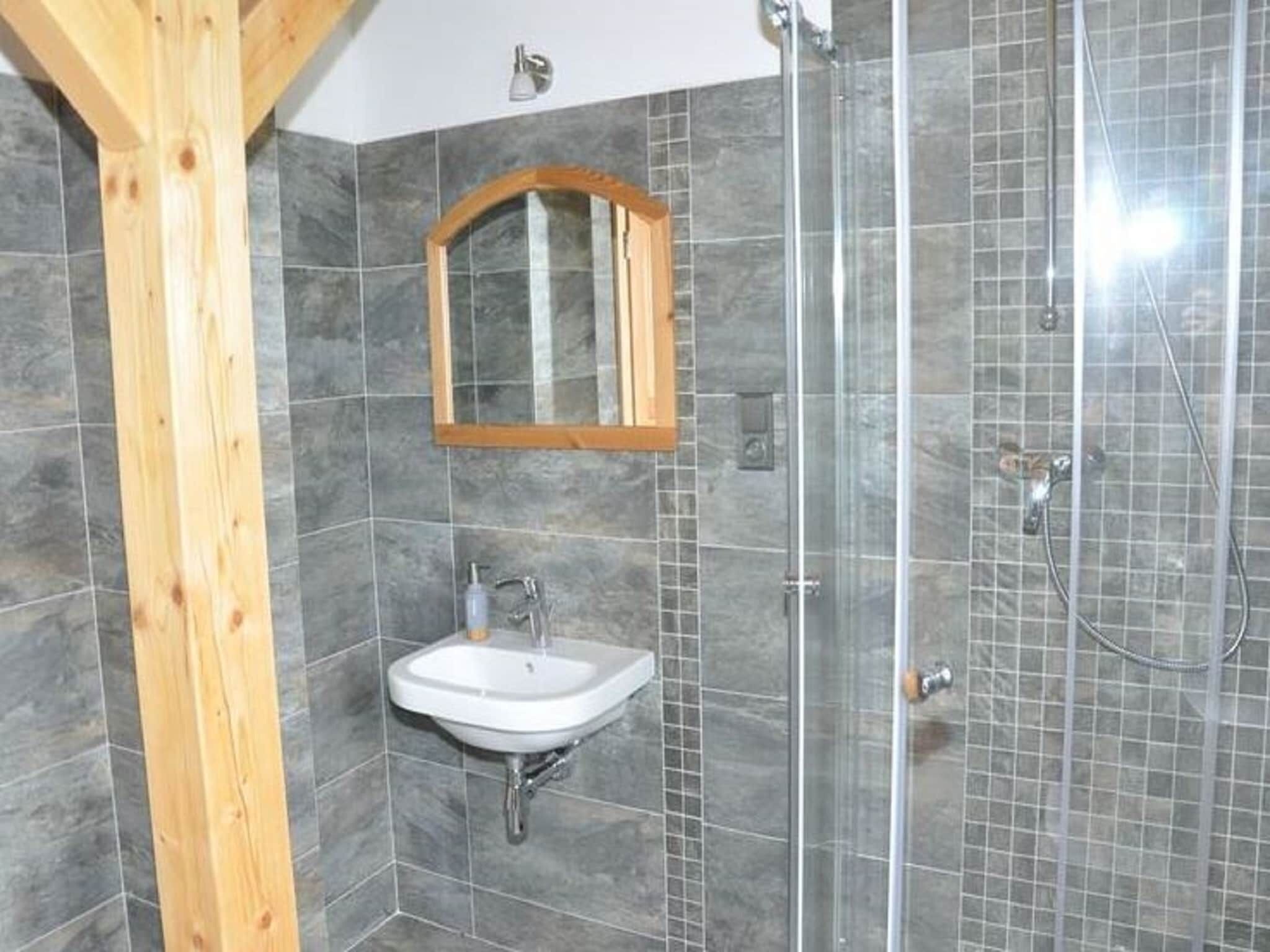 Ein Badezimmer mit Holzbalken, einem Waschbecken, einem Spiegel und einer Dusche.