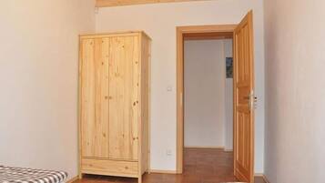 A room with two beds, a wooden wardrobe, and a door leading to another room.
