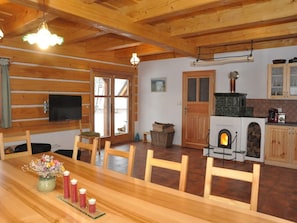 A wooden interior with a fireplace, dining table, chairs, and a television.