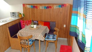 A dining area with a table set for two, wooden chairs, a bench, and a small kitchen area with a microwave. - Spacious cottage in the Giant Mountains, 1 km from the skislopes (Jestřabí V Krkonoších)