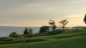 A grassy area with a bench and trees near a body of water. - Walk to beach, cozy, lovely room in "Kingsmill on the James" (Williamsburg)