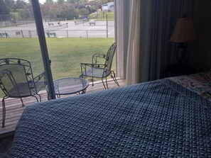 Un balcón con una cama, dos sillas y vista a una cancha de tenis.