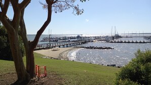 A coastal marina with boats docked, a pier extending into the water, and a grassy area with a tree in the foreground. - Walk to beach, cozy, lovely room in "Kingsmill on the James" (Williamsburg)