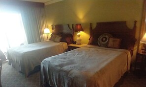 Habitación de hotel con dos camas, una mesita de noche, una lámpara y una ventana con cortinas.