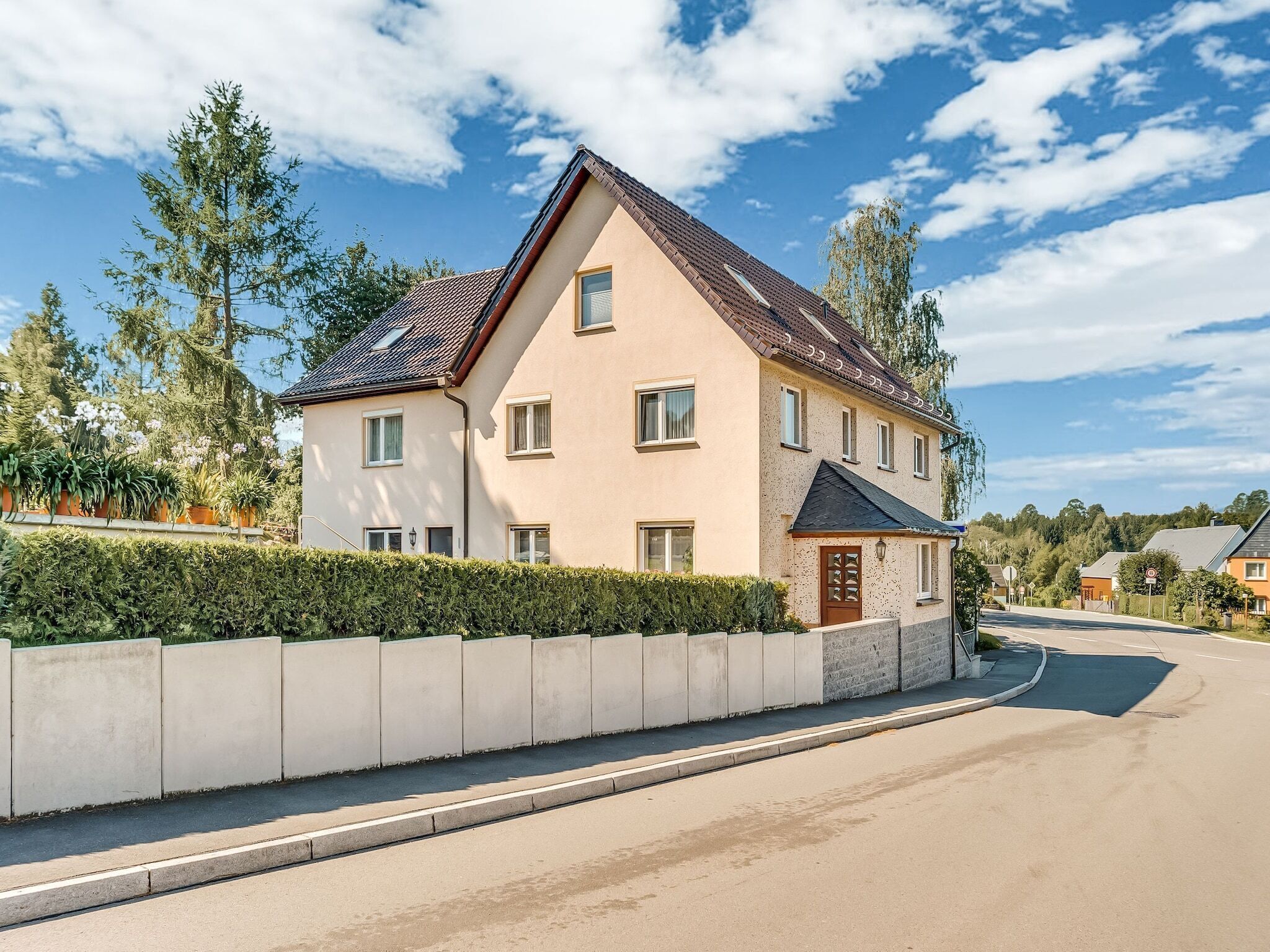 Ein zweistöckiges Haus mit Satteldach, einer Veranda und einer Auffahrt.