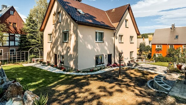 A two-story house with a sloped roof, a small front porch, and a well-maintained garden with a stone pathway and flower beds. - Tranquil Stay in Dörnthal (Pfaffroda Ot Dörnthal)