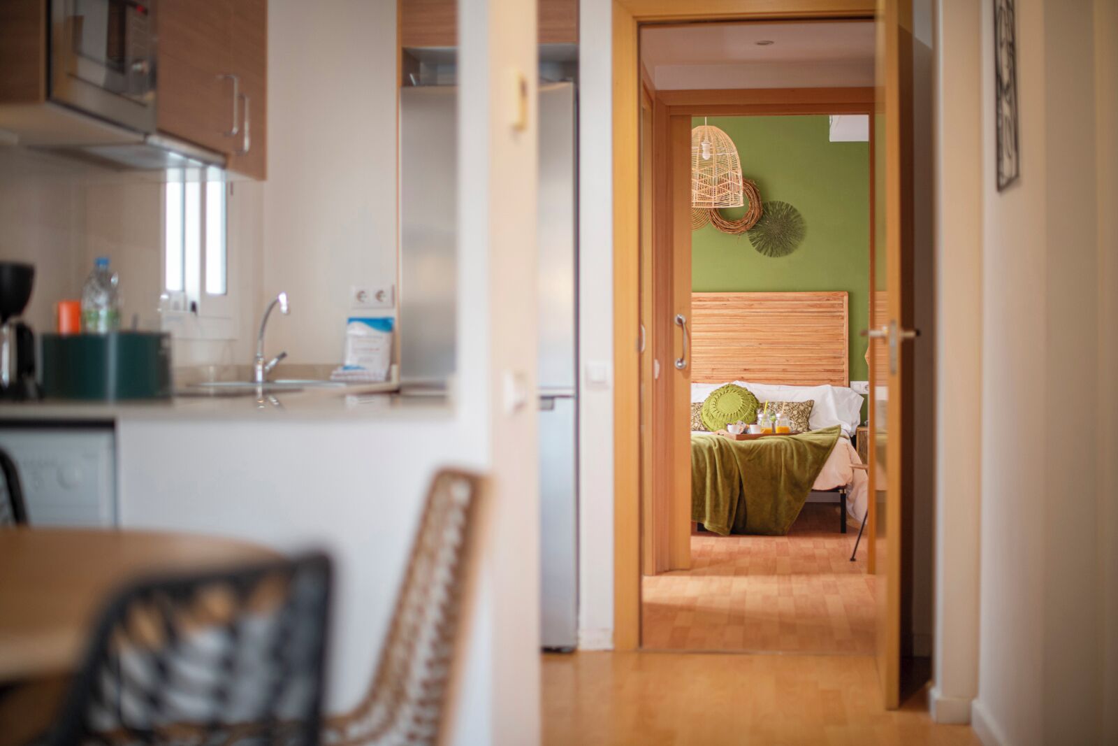 Una cocina moderna con comedor, una cama con cabecera verde y una lámpara colgante de mimbre.