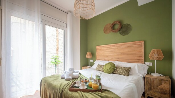 Un dormitorio ordenado con una cama grande, una mesita de noche con lámpara y una bandeja con alimentos para el desayuno.