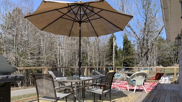 Un patio exterior con mesa y sillas, una parrilla y un gran paraguas.