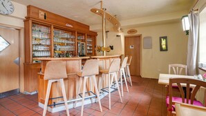 A bar area with a wooden bar counter, multiple stools, and a glass display case filled with bottles. - Flat in Meisberg with in-house catering (Meisburg)