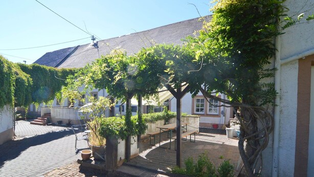 A cobblestone street with buildings on either side, some with vines. There are benches and a small garden area. - Flat in Meisberg with in-house catering (Meisburg)