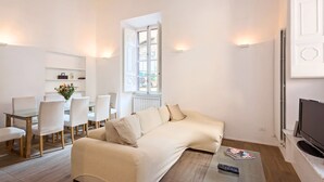 Un salon moderne avec un canapé beige, une table basse en verre et un coin repas avec des chaises blanches.