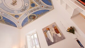 Une pièce dotée d’un plafond haut, ornée de fresques décoratives, et comprenant une grande fenêtre ainsi qu’une peinture abstraite moderne.
