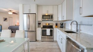 A modern kitchen with stainless steel appliances, white cabinetry, and a glass dining table. - Marvelous Views & Steps From The Beach 1608 (Bonita Springs)