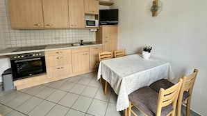 Cocina compacta con armarios de madera, microondas, estufa y una mesa de comedor con sillas.