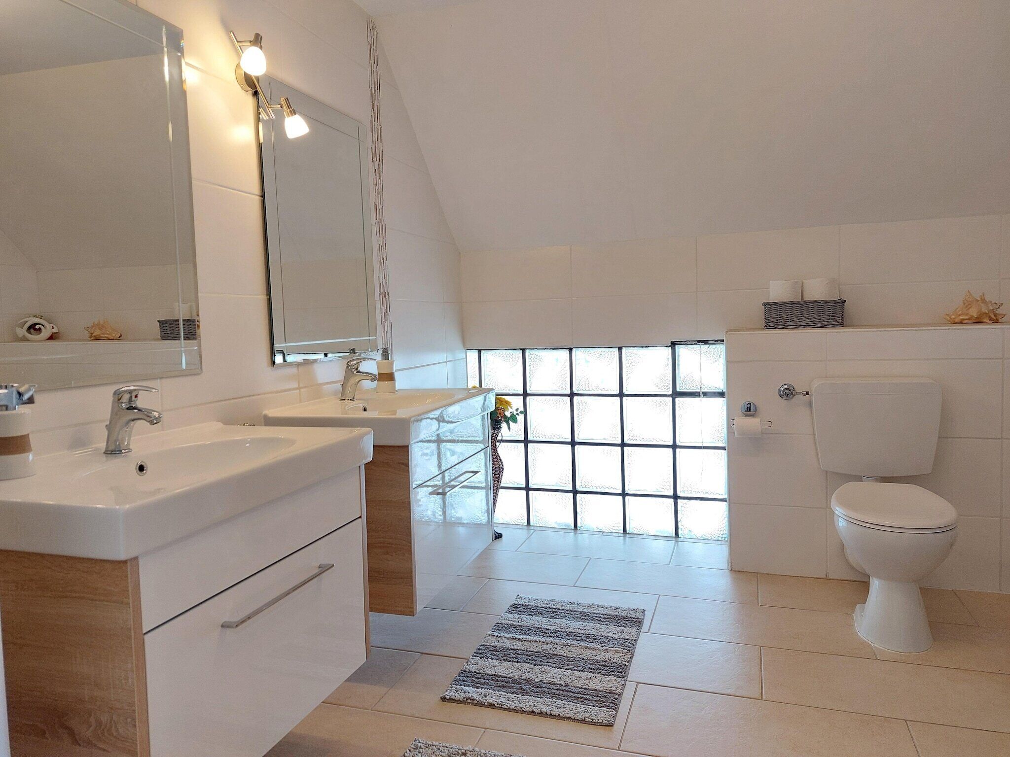 Une salle de bain moderne avec un grand miroir, deux lavabos, des toilettes et une fenêtre en verre dépoli.