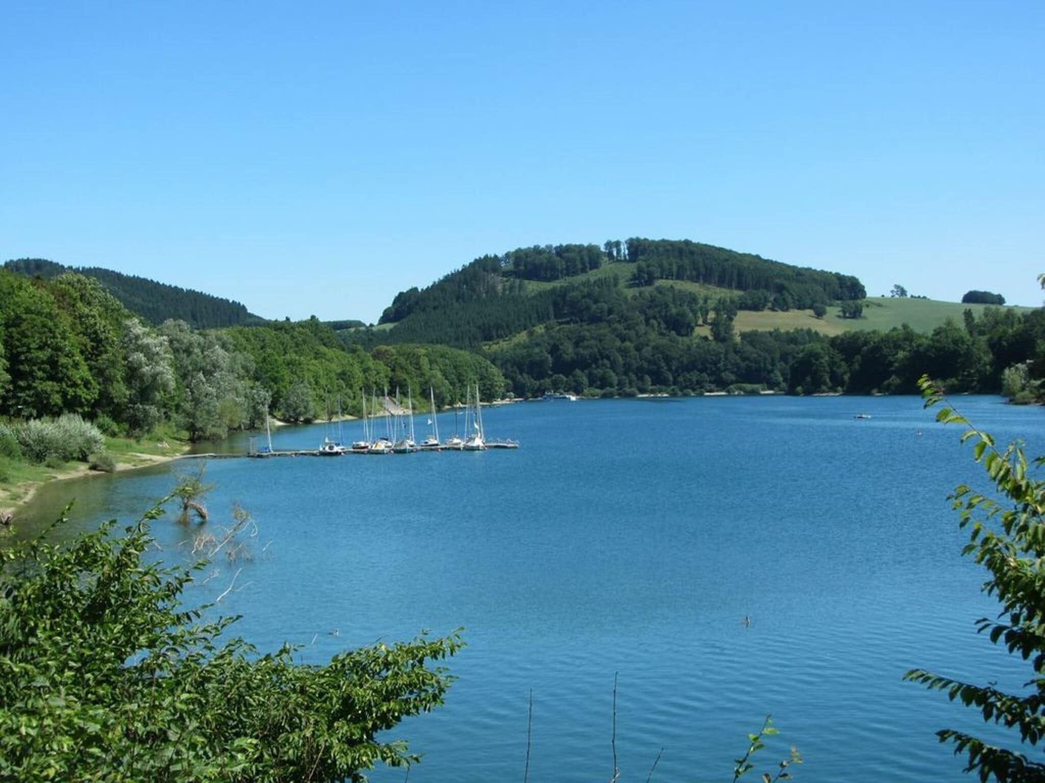 Un lago tranquillo con barche ormeggiate sulla riva, circondato da vegetazione lussureggiante e colline.