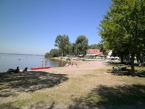 A beach with a grassy area, a red kayak, and a building with a red roof in the background.