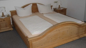 A wooden double bed with two pillows, a nightstand with a lamp, and a bedside table. - Ferienwohnung, Ingenried (Ingenried)