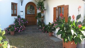 A courtyard with a cobblestone path leading to a wooden door, surrounded by potted plants and flowers. - Ferienwohnung, Ingenried (Ingenried)