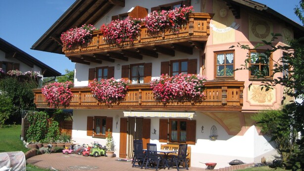 A traditional chalet with wooden balconies, a patio with outdoor seating, and a garden area. - Ferienwohnung, Ingenried (Ingenried)