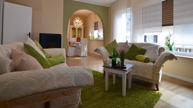 Een woonkamer met twee banken, een salontafel en een open haard. Achtergrond toont een eethoek met een kroonluchter.