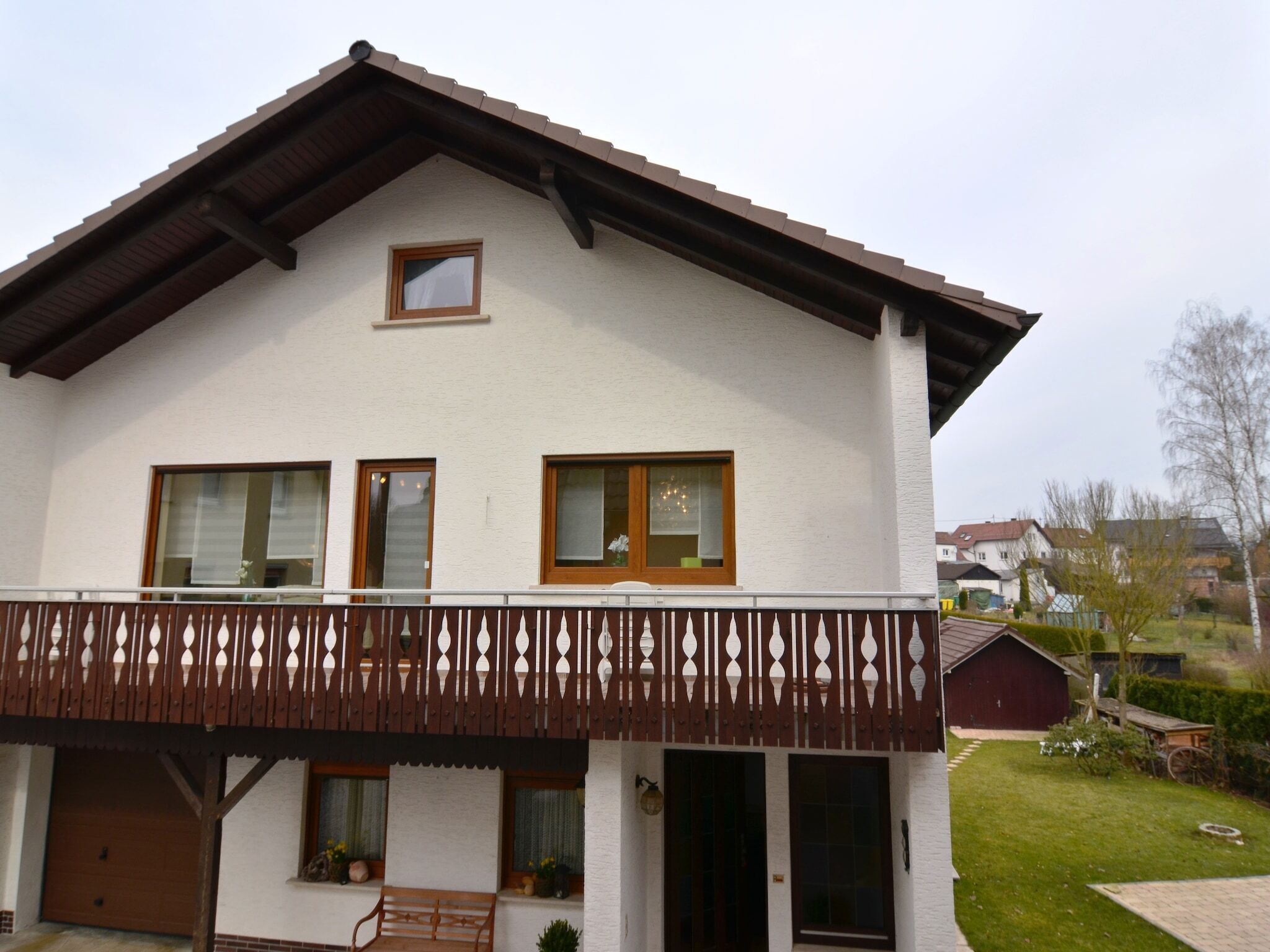 Ein zweistöckiges Haus mit Balkon, Garage und kleinem Garten.