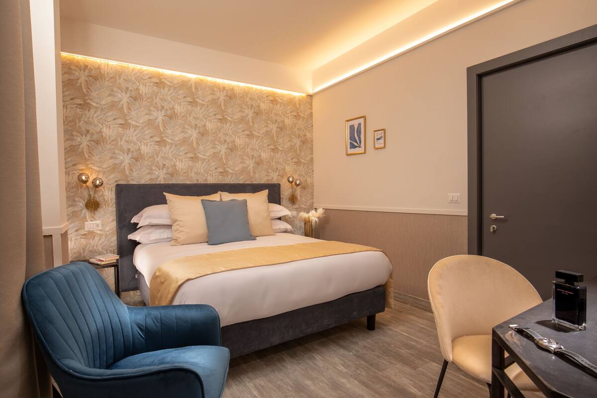 A hotel room with a large bed, two chairs, a small table, and a door.