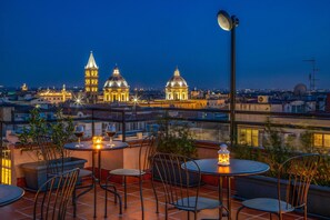 An outdoor terrace with tables and chairs, overlooking a cityscape with illuminated buildings. - Sophie Terrace Hotel (Rome)
