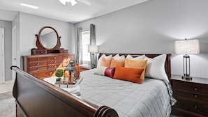 Une chambre à coucher avec un lit en bois, une commode, un miroir, une table de chevet et un ventilateur de plafond.