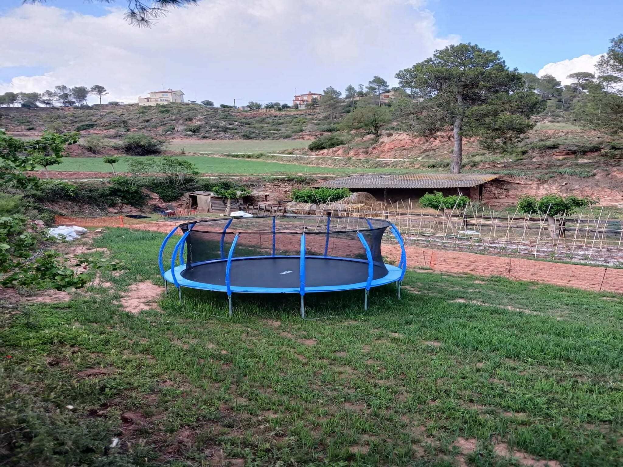 Un trampolín en un área con césped, con vista a un paisaje montañoso y edificios al fondo.