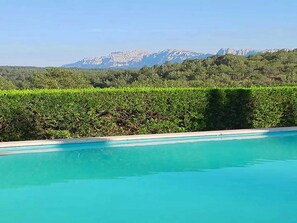 A swimming pool with a view of a mountain range and a hedge in the foreground. - Belvilla by OYO Mas Set Rengs (Sant Salvador de Guardiola)