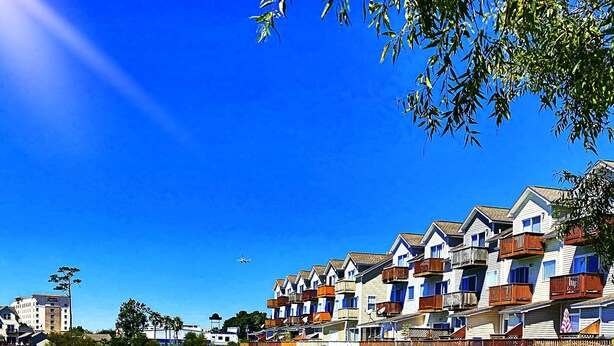 Ein Hotel am Wasserufer mit mehrstöckigen Gebäuden, einem Holzsteg und blauem, wolkenlosem Himmel.