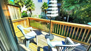 Eine Holzterrasse mit zwei weißen Plastikstühlen und einem gestreiften Sonnenschirm.