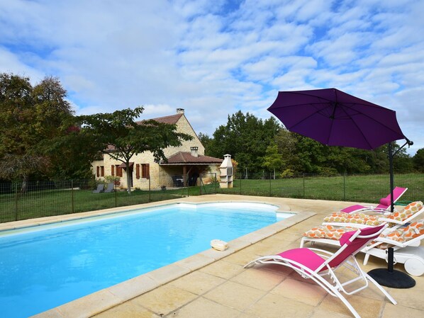 Relax by the pool surrounded by a fence, lounge chairs, and a shaded area.