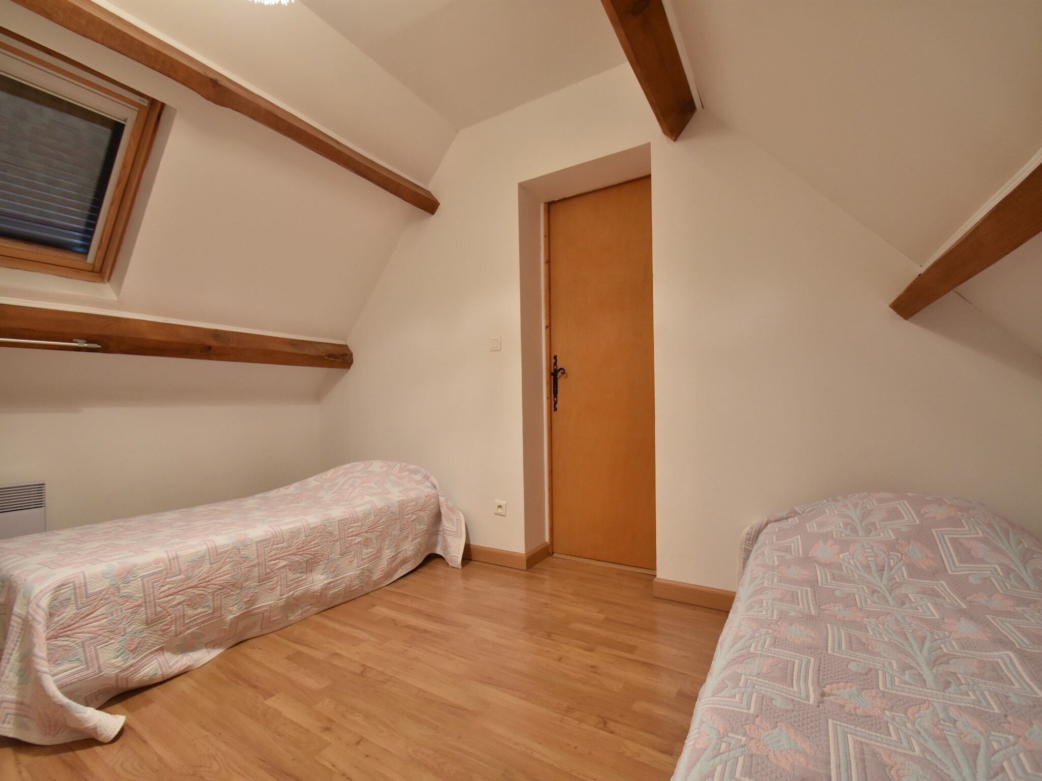 Ein kleines Zimmer mit zwei Betten, Holzbalken, einem Fenster und einer Tür.