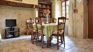 A dining area with a table set for four, surrounded by wooden chairs, a television on a stand, and a stone wall. - Spacious holiday home with private pool (Uzech)