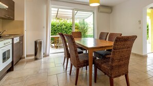 A modern kitchen with a dining area, featuring a large table and wicker chairs, a built-in oven, and a trash bin.